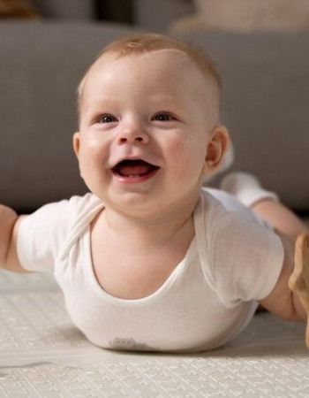 Un bébé souriant allongé au sol avec un hochet 