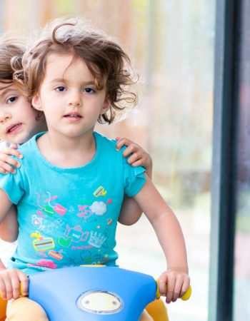 Deux enfants sur un tricycle à l'extérieur de la crèche