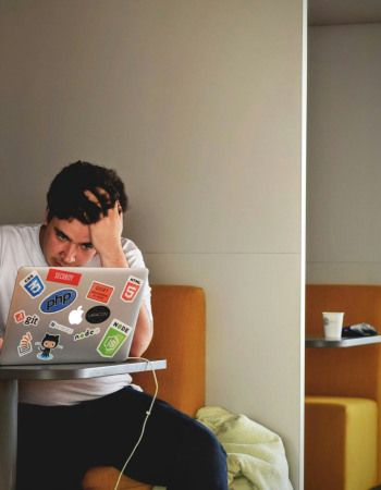 Photo d'une personne assise à un bureau, face à son ordinateur, se tenant la tête