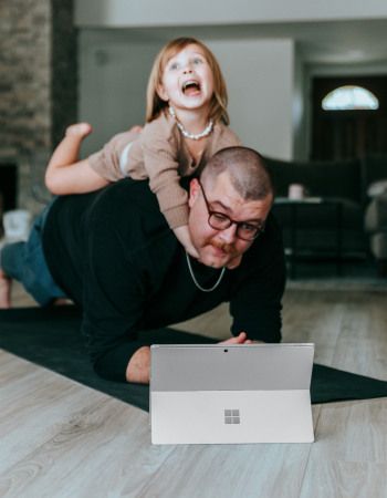 Un père qui regarde sa tablette avec une petite fille sur son dos