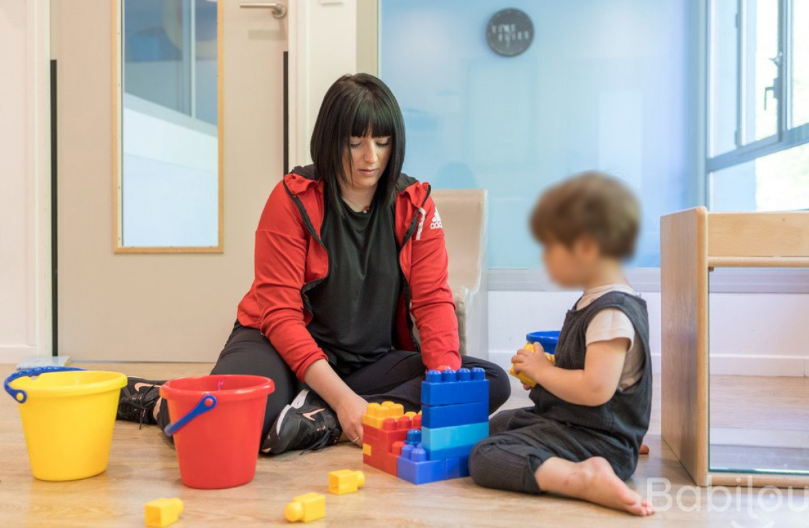 Une professionnelle de la petite enfance joue avec un enfant sur un atelier de construction.