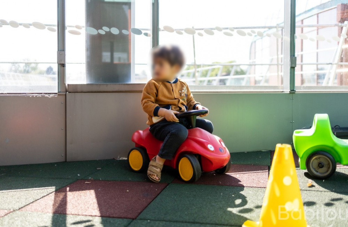 Un enfant fait du trotteur dans l'espace extérieur de la crèche. 