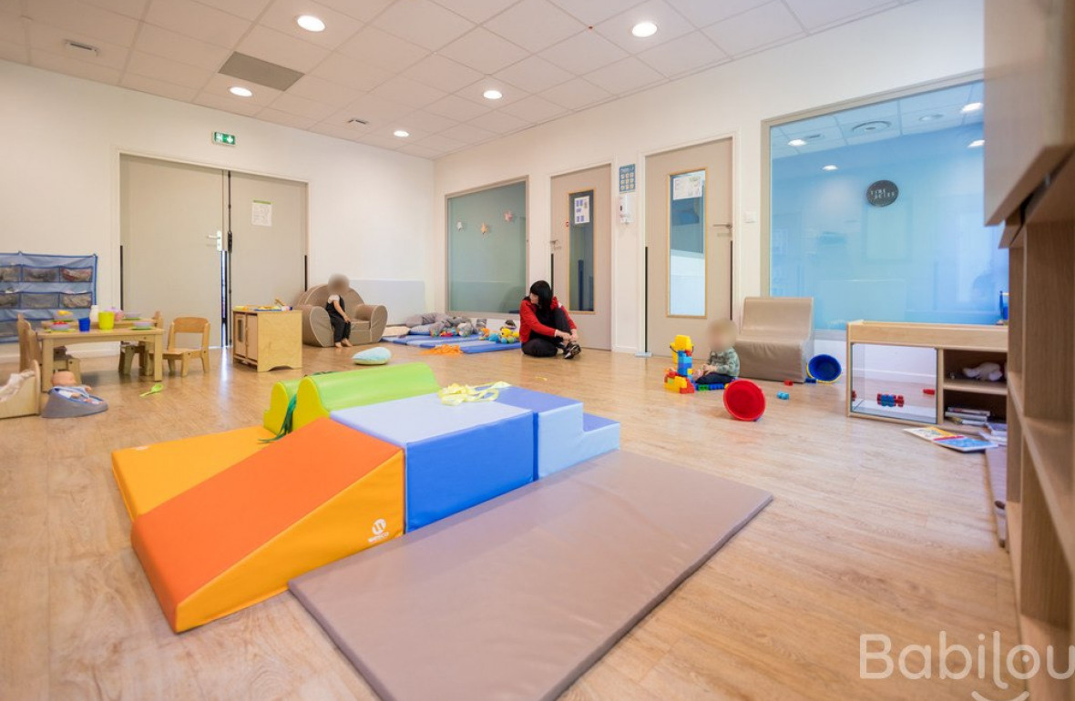 Les enfants jouent dans la salle de jeux de la crèche sous le regard attentif d'une professionnelle de la petite enfance.