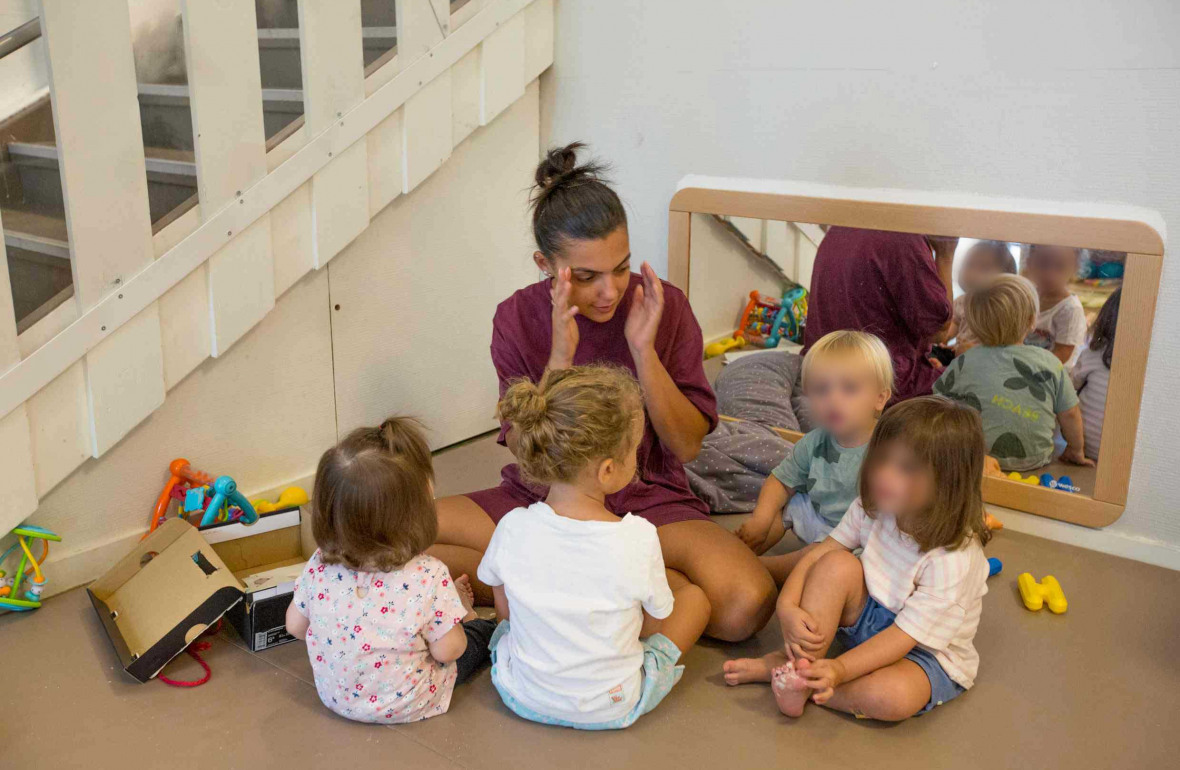 Une professionnelle en crèche assise entouré d'un groupe d'enfant 