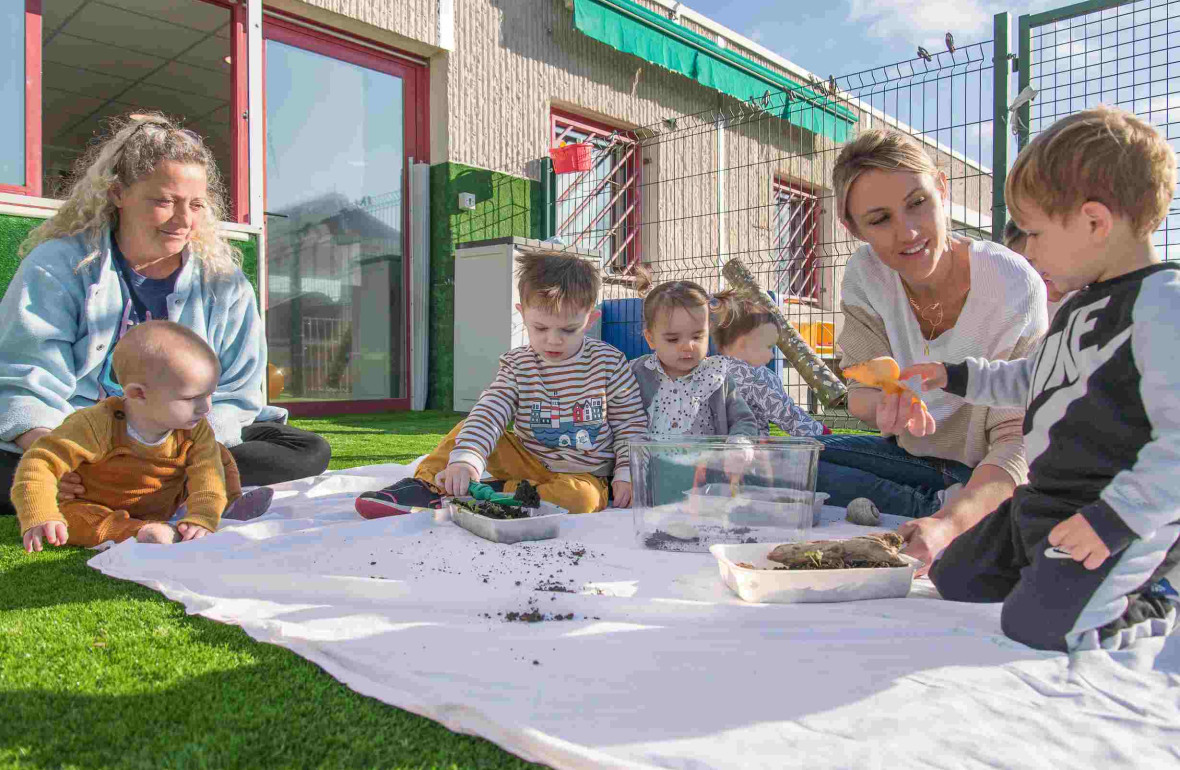 Un groupe d'enfant en crèche et deux pro jouant dans le jardin