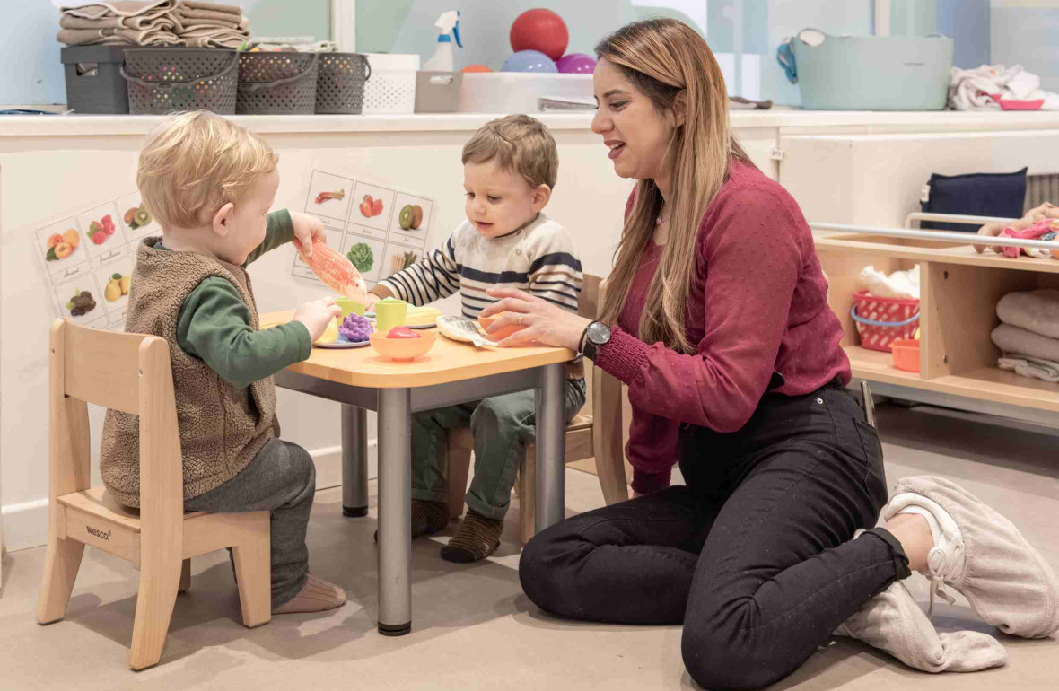 Une professionnelle en crèche assise entouré de deux d'enfant 