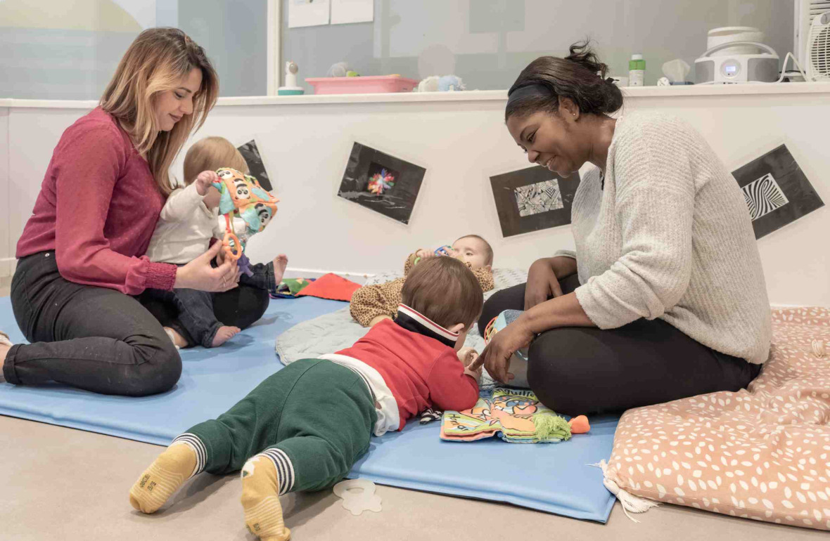 Deux pro en crèche avec deux enfants sur un tapis d'éveil 