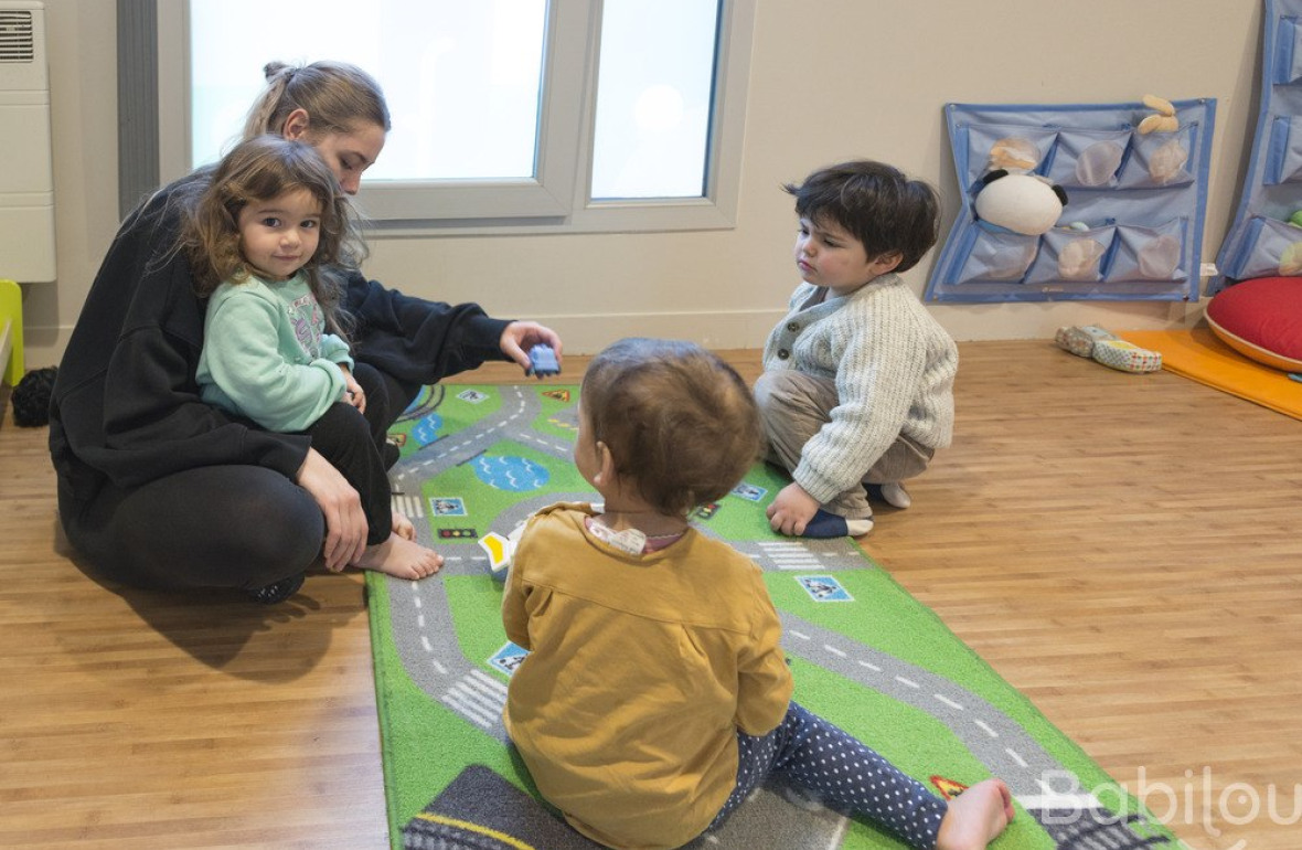 Une professionnelle en crèche assise entouré d'un groupe d'enfants 