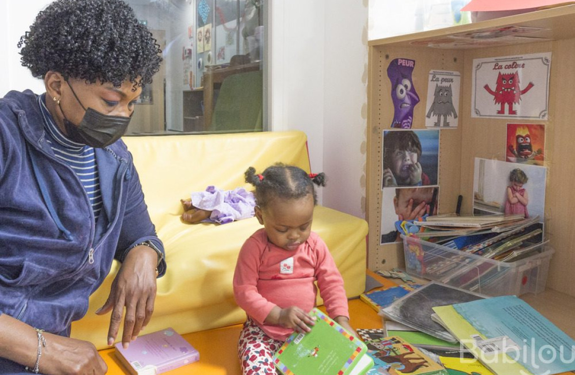 Une professionnelle en crèche qui lit un livre à une enfant