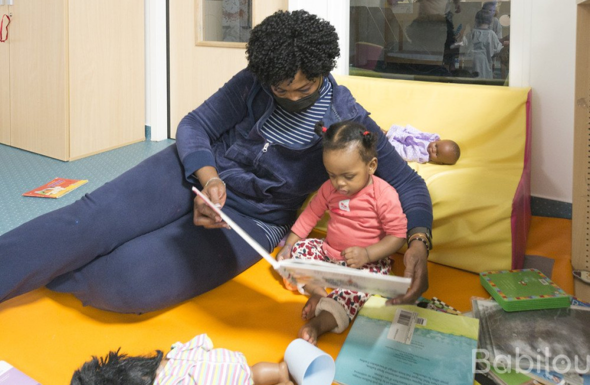 Une professionnelle en crèche qui lit un livre à une enfant