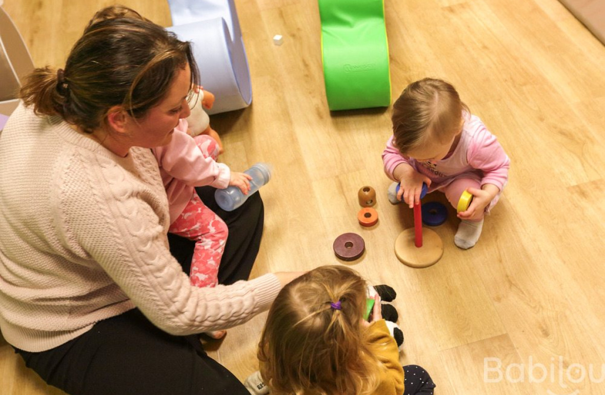 Une professionnelle en crèche assise entouré d'un groupe d'enfants