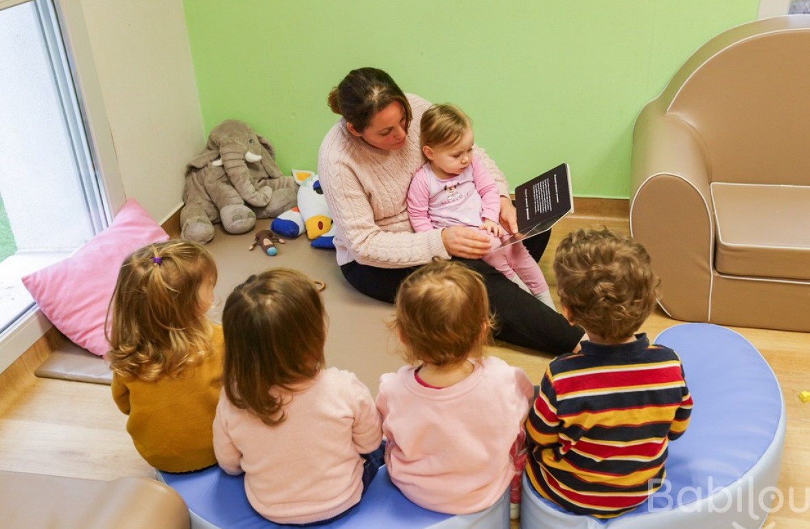 Une professionnelle en crèche qui lit un livre à une enfants