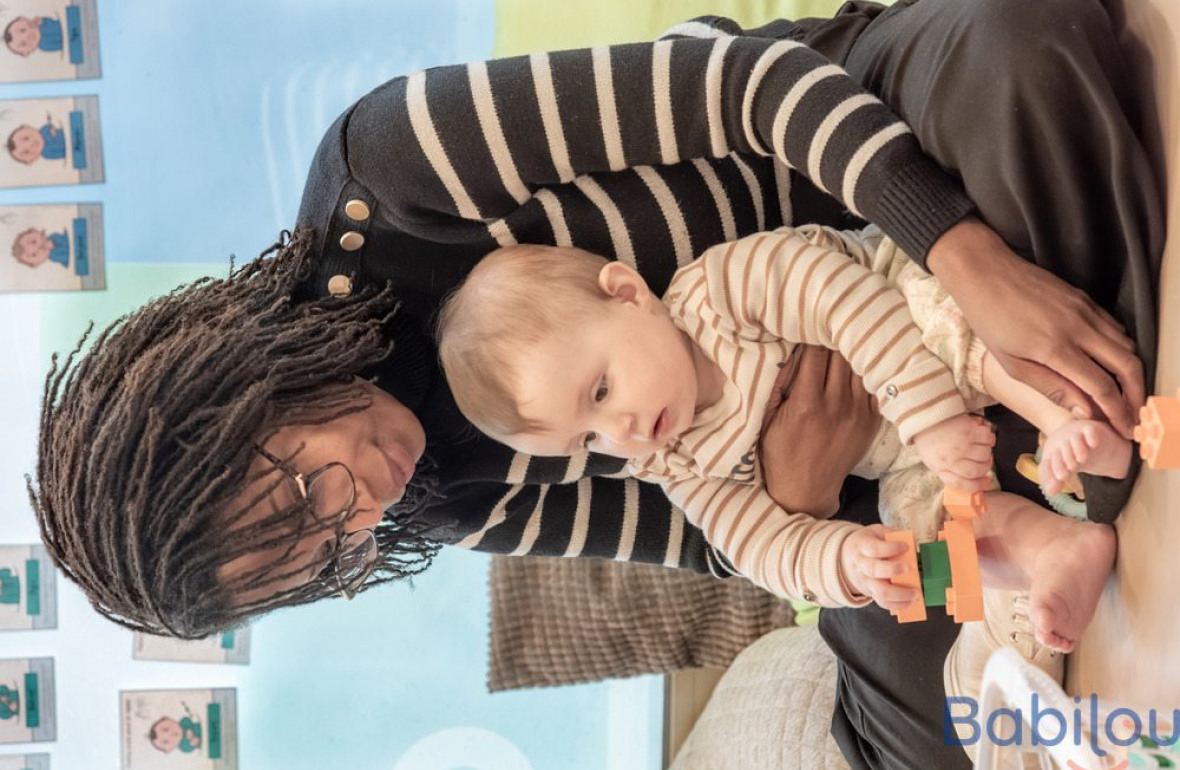 Une professionnelle en crèche assise avec un bébé