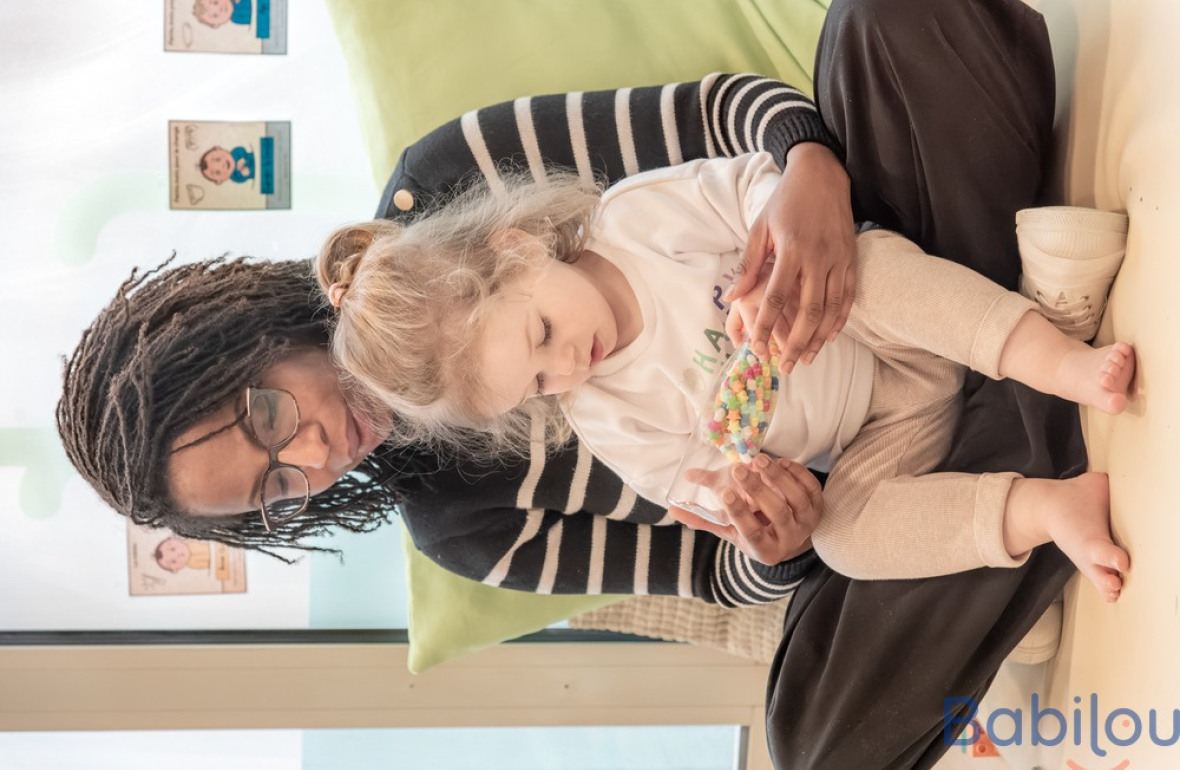 Une professionnelle en crèche assise avec un enfant