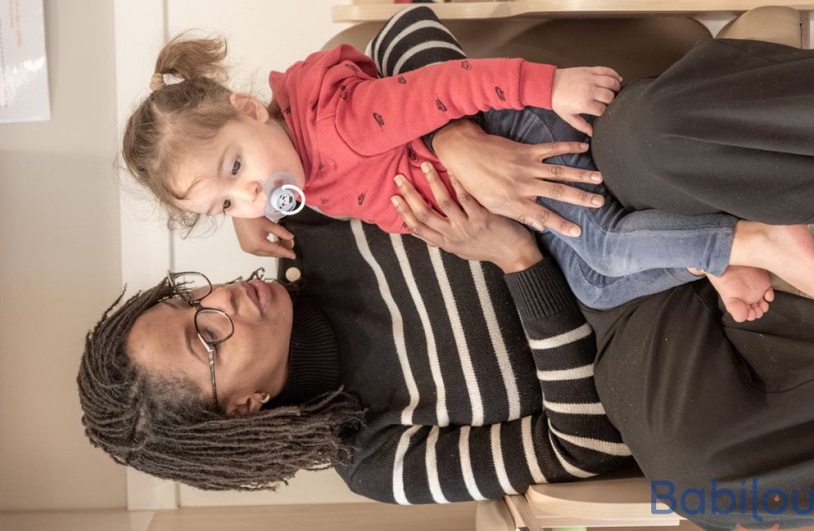 Une professionnelle en crèche assise avec un enfant