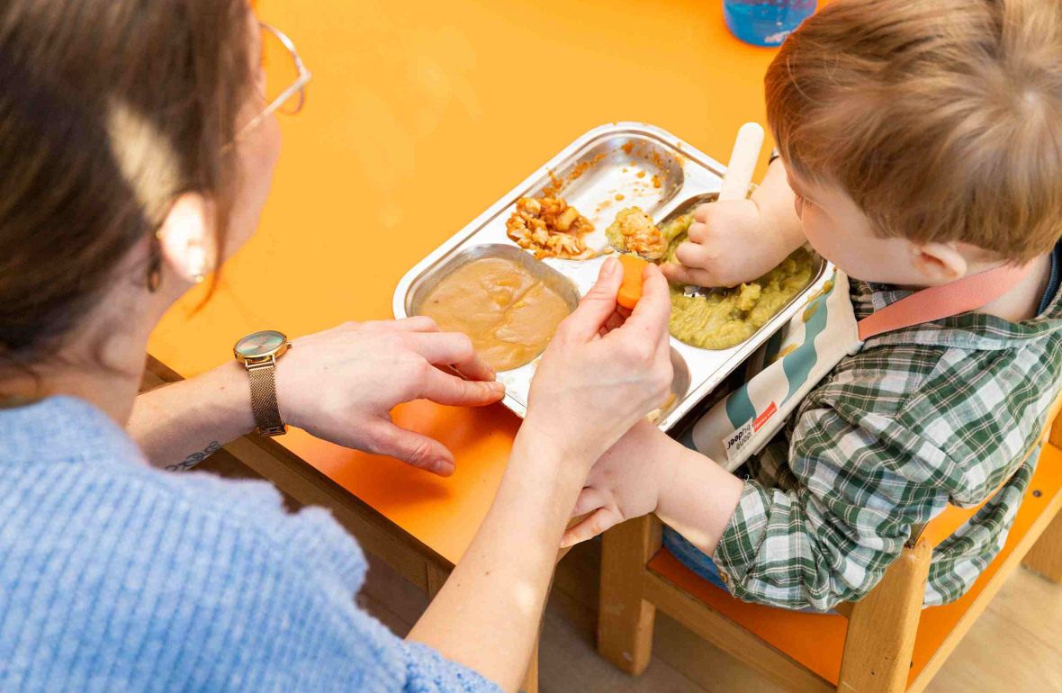 Une pro en crèche qui donne à manger à un enfant