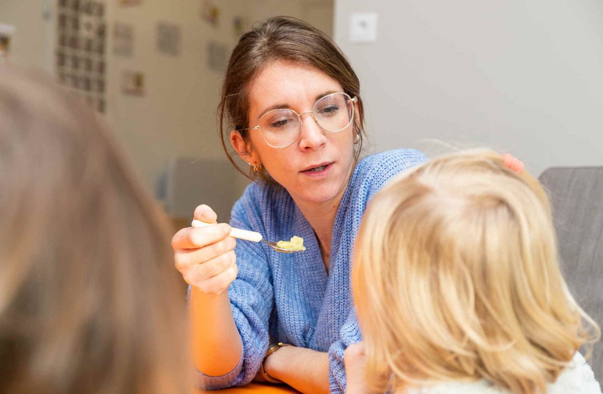 Une pro en crèche qui donne à manger à un enfant
