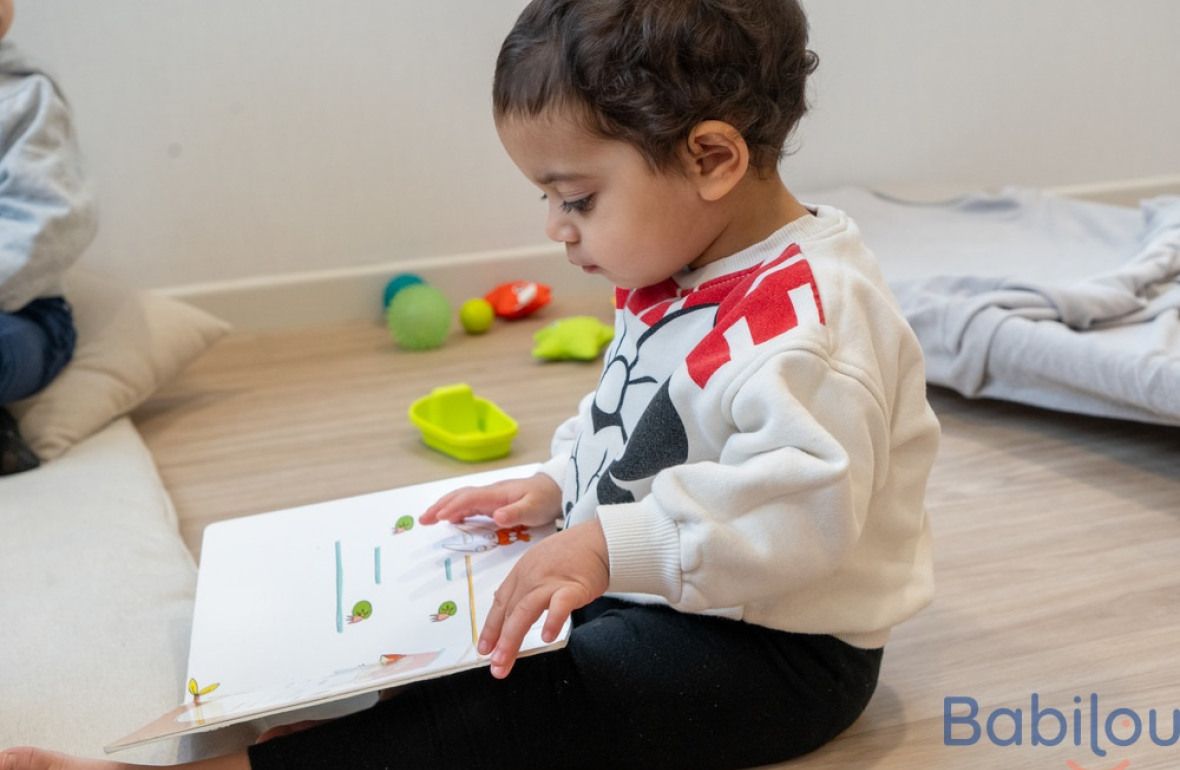 Un enfant en crèche Babilou qui regarde un livre 