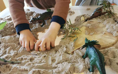 Un petit garçon jouant dans une boîte rempli de sable avec des jouets en forme de dinosaure 