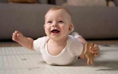Un bébé souriant allongé au sol avec un hochet 