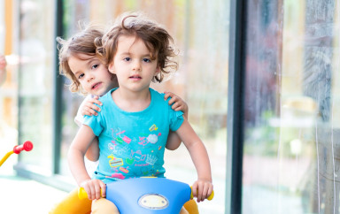 Deux enfants sur un tricycle à l'extérieur de la crèche