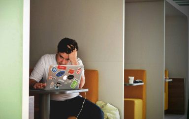 Photo d'une personne assise à un bureau, face à son ordinateur, se tenant la tête