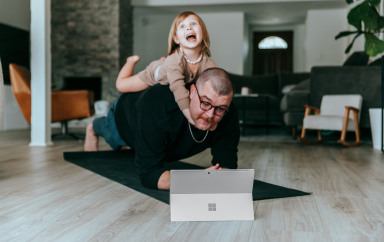 Un père qui regarde sa tablette avec une petite fille sur son dos