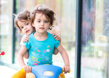 Deux enfants sur un tricycle à l'extérieur de la crèche