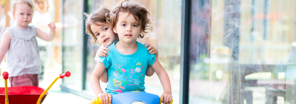 Deux enfants sur un tricycle à l'extérieur de la crèche