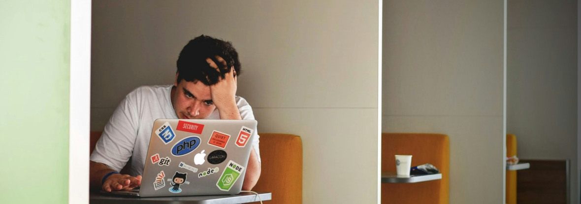 Photo d'une personne assise à un bureau, face à son ordinateur, se tenant la tête