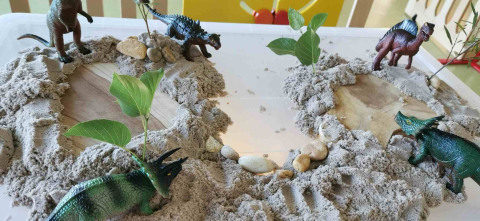 Une mise en scène avec des jouets dinosaures dans un décor avec des pierres et du sable 