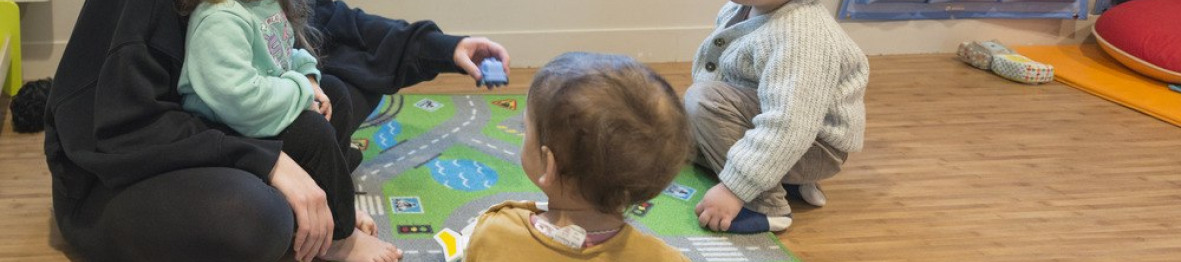 Une professionnelle en crèche assise entouré d'un groupe d'enfants 