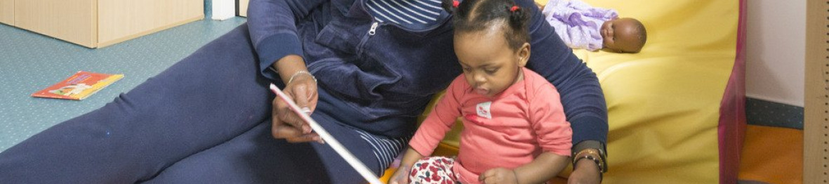 Une professionnelle en crèche qui lit un livre à une enfant