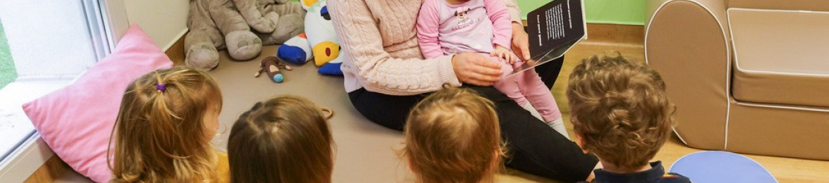 Une professionnelle en crèche qui lit un livre à une enfants