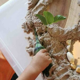 Enfant jouant avec du sable et des feuilles et jouets en forme de dinosaures