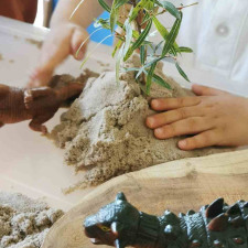 Un petit garçon jouant dans une boîte rempli de sable avec des jouets en forme de dinosaure 