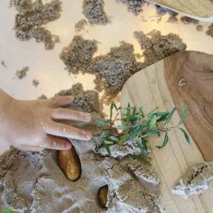 Une boite sensorielle fabriquée avec du sable et des feuilles, rempli de jouets dinosaures