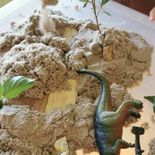 Une boîte rempli de sable avec un jouet en forme de dinosaure 