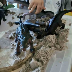 Un petit garçon jouant dans une boîte rempli de sable avec des jouets en forme de dinosaure 